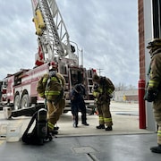 Des pompiers attachent leur équipement derrière un camion de pompier. 