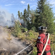 Un pompier forestier arrose un feu de forêt.