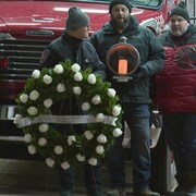 Des pompiers devant un camion, l'un deux tient une couronne de roses.