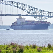 Un navire marchand rempli de conteneurs, accompagné d'un petit bateau d'aide à la navigation.