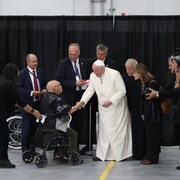 Le pape François serre la main d'un homme en fauteuil roulant.