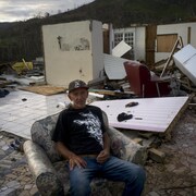 Un homme assis dans un fauteuil devant sa maison détruite.