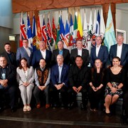 Deux rangées de personnes assises devant les drapeaux des territoires et des provinces du Canada.
