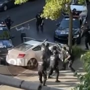 Silya Medkour (gauche de l'écran), qui lève les mains en l'air, et son présumé complice, Ben Terry Edouard (droite de l'écran), entourés de policiers et entre des voitures de police.