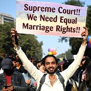 Un homme tient une pancarte en appui au mariage homosexuel, entouré de ballons arc-en-ciel.