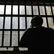 Un détenu regarde par une fenêtre munie de barreaux.