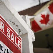 Une pancarte de vente devant une maison où flotte un drapeau canadien.
