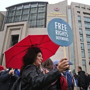 Une femme tient une petite pancarte sur laquelle on peut lire : « Défenseurs des droits de la personne ».
