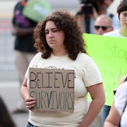 Une manifestante tient une pancarte indiquant « Believe survivors » (« Croyons les survivantes »). 