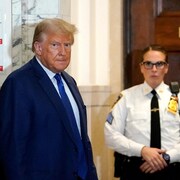 Donald Trump regarde en direction du photographe tandis qu'on voit une agente de sécurité à l'arrière.