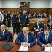 Donald Trump, les yeux fermés,  assis dans la salle d'audience entouré de ses avocats.