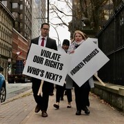 Un homme en veston-cravate et une femme mènent une marche avec des pancartes à la main.