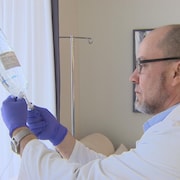 Un homme habillé d'un sarrau manipule une préparation médicamenteuse liquide.