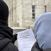 Deux &eacute;tudiantes voil&eacute;es regardent une copie du projet de loi 9 devant un pavillon de l'Universit&eacute; de Montr&eacute;al