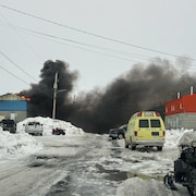 Un bâtiment en flammes, d'où se dégage une importante fumée noire. La rue est enneigée.
