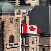 Extérieur en pierres de l'Assemblée législative de l'Ontario avec un drapeau canadien en avant-plan.
