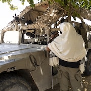 Un homme debout devant un véhicule militaire.