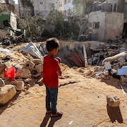 Un enfant est debout devant les débris d'un bâtiment.