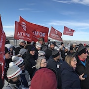 Quelques dizaines de personnes, à l'extérieur, sont rassemblées avec des drapeaux d'Unifor.