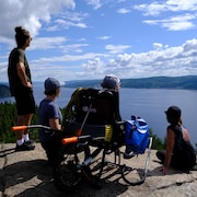 Quatre personnes, dont une en fauteuil roulant adapté, observent la baie des Ha! Ha! du haut du sentier Eucher, à La Baie.