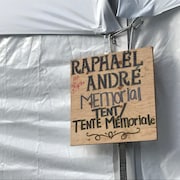 Un panneau en bois sur lequel on peut lire : ''Raphaël André (aka Napa) Memorial Tent/Tente Mémoriale''.