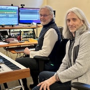 Dave Lawlor (à gauche) et Michel Chammartin (à droite), membres du groupe La Raquette à claquettes, sont assis dans un studio d'enregistrement. Ils sont entourés d'équipements de musique, avec des écrans montrant des logiciels de mixage sonore.