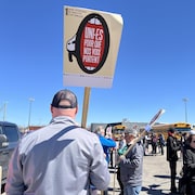 un  homme tient une pancarte de dos devant une foule rassemblée dans un stationnement