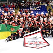 Les joueuses des Rebels de Regina, vêtues de leurs chandails aux couleurs noir, jaune et rouge, posent avec leur bannière de championnes et le drapeau de la Saskatchewan.