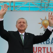 Le président Erdoğan, les deux bras en l'air, est debout sur une scène.
