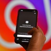 Un téléphone intelligent affiche la fonctionnalité Reels, devant un logo géant d'Instagram. 