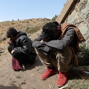 Des hommes accroupis sur le flanc d'une colline  
