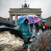 Un demandeur s'asile sous la pluie devant la porte de Brandebourg, à Berlin.