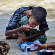 Un enfant en train de manger, assis à même le sol.