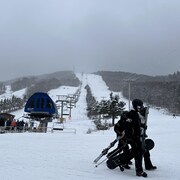 Des skieurs en train de marcher, leurs ski ou leur planche à neige à la main, en train de marcher au bas d'une piste.