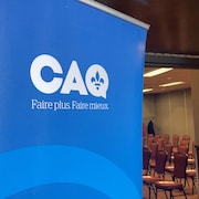 Une affiche de la CAQ près d'une salle ayant des chaises vides.