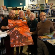 Une équipe sourit en tenant une affiche dans une librairie.