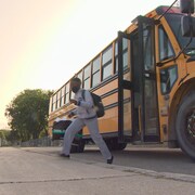 Un élève quitte un autobus scolaire pour se rendre dans une cour d'école dans la lumière du matin.