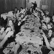 Guides, hôtesses et autres membres du personnel des relations publiques de Radio-Canada attablés à une longue table devant un repas traditionnel des Fêtes.