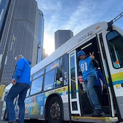 Un partisan habillé avec un chandail d'une équipe de la NFL fait un signe de paix en débarquant d'un autobus municipal de Windsor arrêté à Détroit.