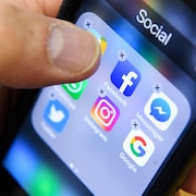 Un homme tient un téléphone intelligent avec les icônes des applications de réseaux sociaux Facebook, Instagram et Twitter vues sur l'écran.