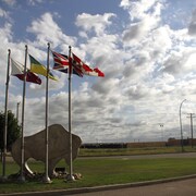 Une sculpture d'un bison ainsi que les drapeaux du Canada, du Royaume-Uni, de la Saskatchewan et de la communauté de Muskeg Lake.