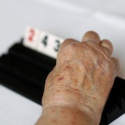 La main d'une femme très âgée replace sur un chevalet les plaques numérotées d'un jeu de rummi. 