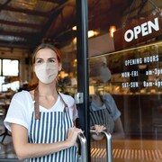 Une femme portant un masque ouvre la porte d'un café.