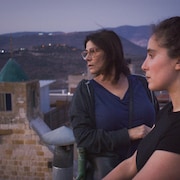 Deux femmes regardent vers l'horizon sur le toit d'une maison. 