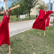 Des robes rouges sont accrochées à des croix de bois.