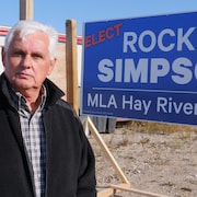 Rocky Simpson se tient devant son affiche de campagne. 