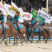 Plusieurs femmes à dos de cheval en tenant des drapeaux. 