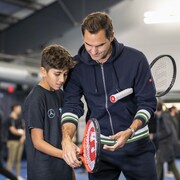 Un homme aide un jeune à tenir sa raquette de tennis.