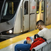 Un homme consulte son téléphone sur le quai du métro.