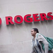 Une femme marche devant un mur avec le nom et le logo de Rogers sur le mur.